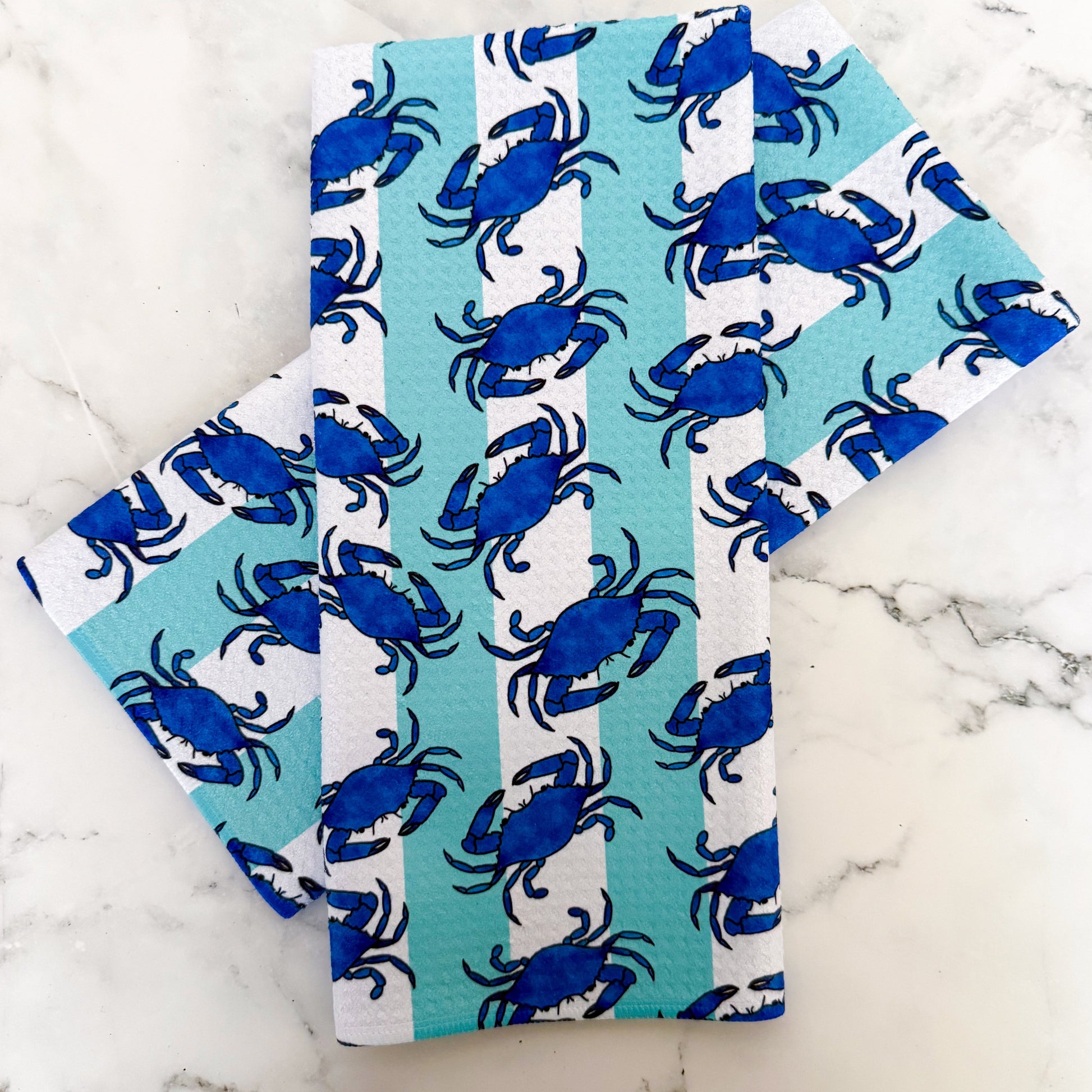 Two folded towels with blue crab pattern on a marble surface