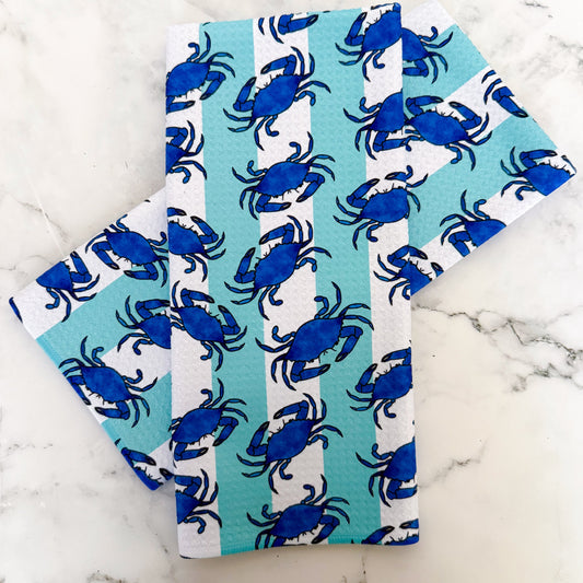 Two folded towels with blue crab pattern on a marble surface